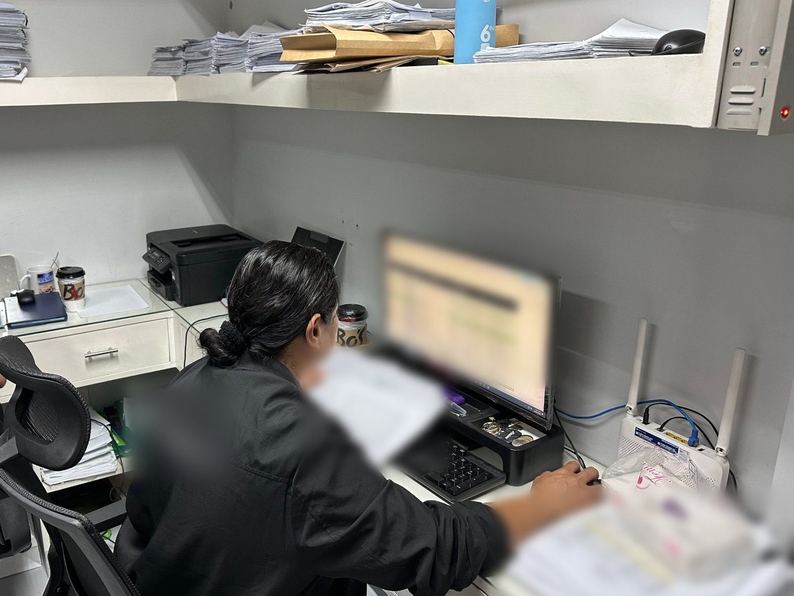 A clerk at the claims desk, a spreadsheet open, shelves of paper claim forms above.